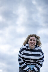 Fototapeta na wymiar A woman laughing loudly outdoors against a background of cloudy sky