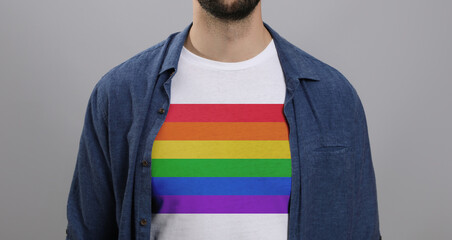 Young man wearing white t-shirt with image of LGBT pride flag on light grey background, closeup