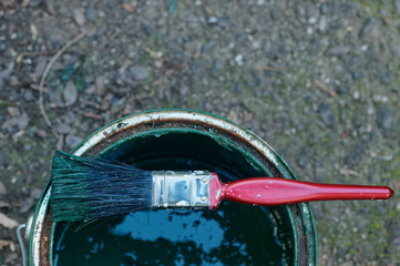 A paint brush sits across the top of a paint can, its bristles have been coloured dark green by the paint