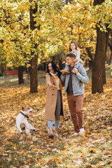 Fototapeta premium Happy young family walks and plays with a dog in the autumn park