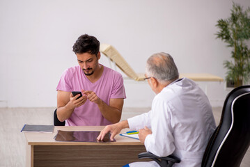 Fototapeta premium Young male patient visiting old male doctor