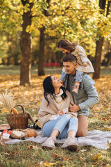 Fototapeta premium Portrait of happy young family sitting on plaid together in autumn park
