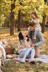 Fototapeta premium Portrait of happy young family sitting on plaid together in autumn park
