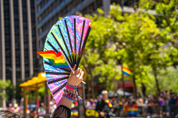 A woman holds a rainbow flag and a fan at the Pride Parade. 