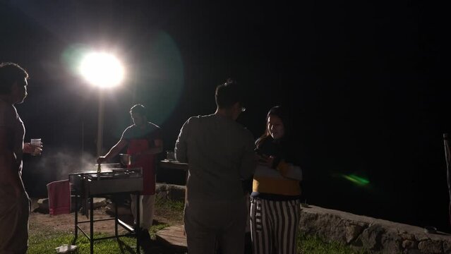male and female friends eating barbecue and having drinks outdoors in a country house in the highlands on the grass at night in 4k 