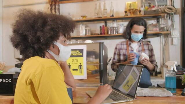 Two young cafe barista partners and entrepreneur work with face mask in coffee shop, waiting for customers order in new normal lifestyle service, SME business impact from COVID-19 pandemic quarantine.