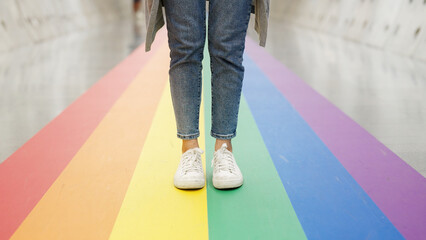 Closeup jeans foot leg white sneaker shoe queer transgender people relax stand on colorful stripes flag line city street lane way. LGBT LGBTQIA gay proud color sign bisexual festival march parade.
