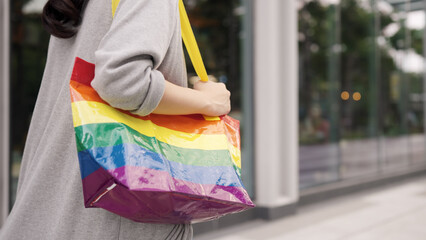 Young adult queer transgender asia gay people carry colorful stripes hold reuse tote bag smile relax walk at city street town. LGBT LGBTQIA culture color sign bisexual enjoy net zero waste eco life.