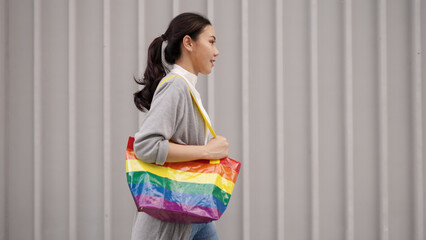 Young adult queer transgender asia gay people carry colorful stripes hold reuse tote bag smile relax walk at city street town. LGBT LGBTQIA culture color sign bisexual enjoy net zero waste eco life.