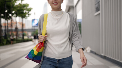 Young adult queer transgender asia gay people carry colorful stripes hold reuse tote bag smile relax walk at city street town. LGBT LGBTQIA culture color sign bisexual enjoy net zero waste eco life.