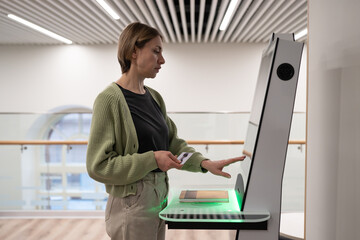 Middle-aged woman using self-service terminal in digital library space, registering book, searching and selecting literature or browsing catalogue. Innovative technologies in libraries