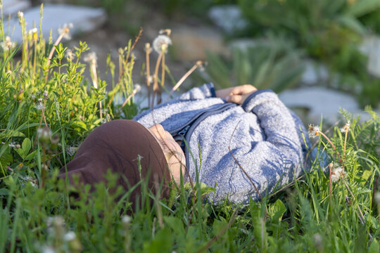 Close up view of a young four year old caucasian child lying on back in a meadow of wildflowers looking up to sky. Little boy daydreaming in nature.