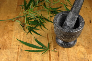marijuana leaves on a wooden table beside a stone mortar