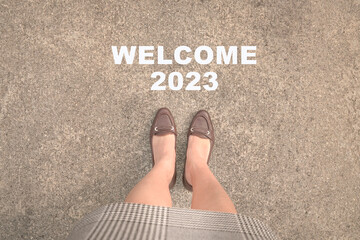 Top view of businesswoman feet with heels standing on asphalt road and text Welcome 2023. Happy new...