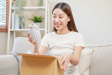 Obraz na płótnie Canvas Happy excited, asian young woman, girl customer sitting on sofa at home, opening and unpacking cardboard box carton parcel after buying ordering present, shopping online, delivery service concept.
