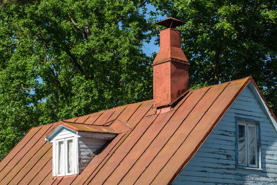 Old tin roof with retro style roof window and red chimney