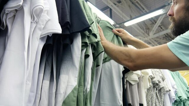 A bearded man choosing a t-shirt in a clothing store