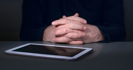 The hands of a mature businessman with a tablet in dark colors