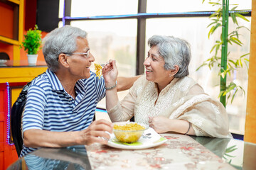 Happy indian senior couple enjoying meal together at home, asian Retired old husband and wife...