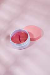 A container with pink eye patches with retinol and collagen on a pink background with a shade