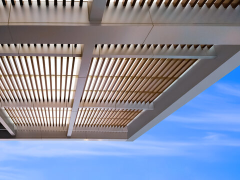 Low angle view of modern battens roof awning outside of building against blue sky background