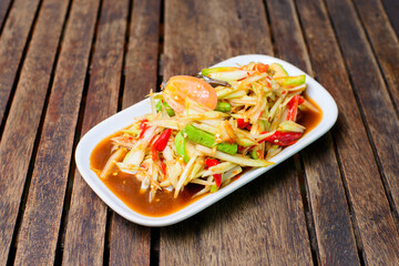Spicy papaya salad with salted crab and fermented fish on the wooden background.