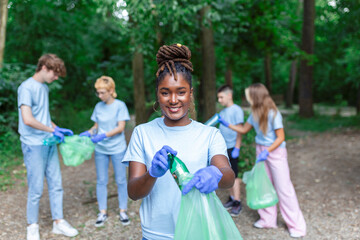 Fototapeta premium Group of young people friends volunteers collecting plastic bottles to trash bags in forest. Ecology concept