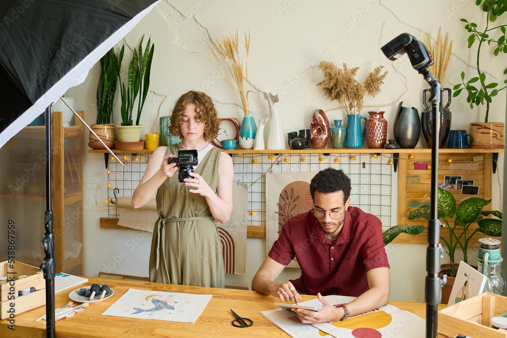 Poster young creative woman taking photo of drawing on table while while standing by black man networking o