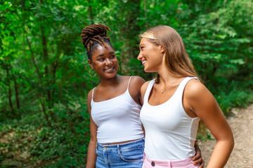 Obraz premium Young smiling women walking and talking while looking at each other outdoor. Happy best friends laughing and having fun.Two women friends sightseeing in summer while on vacation.