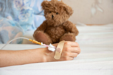 Children's hand with a dropper on the bed and next to it lies a children's teddy bear in the...