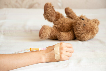Children's hand with a dropper on the bed and next to it lies a children's teddy bear in the...