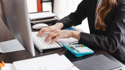 Happy businesswoman wearing suit posing sitting in a desktop at office workspace. - obrazy, fototapety, plakaty