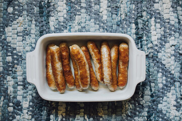 browned, cooked individual breakfast sausage links in white dish on blue placemat, table