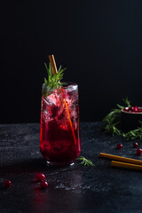 Cranberry drink with ice, decorated with rosemary. Near fresh rosemary and cranberries. Dark key.