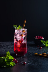 Cranberry drink with ice and a straw in a glass. Fresh mint and cranberries are nearby.
