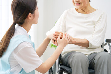 室内で車椅子に乗る高齢者女性と会話する介護士