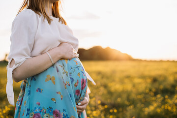 Horizontal close-up photo of a pregnant woman holding the abdomen with both hands. Bright photo at...