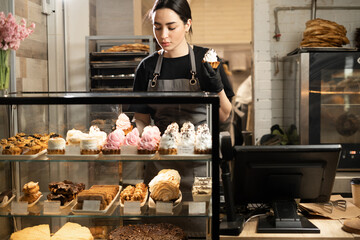 Handsome woman coffee shop employee placing pastry and cake in bakery refrigerator showcase at...