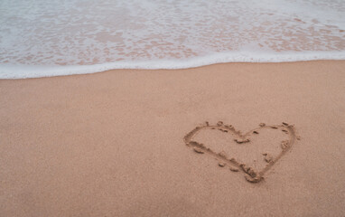 Heart symbol of love hand drawn on sand summer beach.