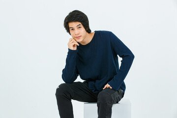 Studio full body shot of Asian young handsome confident slim healthy athletic teenager fashion male model in long sleeve shirt fabric pants and sneaker sitting on box posing on white background
