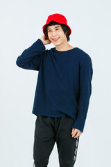 Full body studio shot Asian young handsome slim teenager fashion male model in street style outfit long sleeve shirt standing posing smiling holding hand adjusting red bucket hat on white background