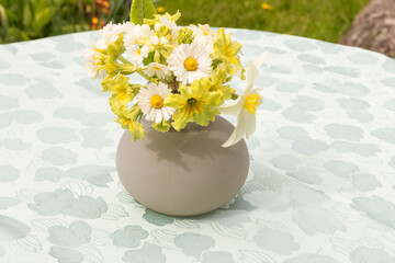 In a glass small vase, a collected fresh bouquet stands on a table in the garden.