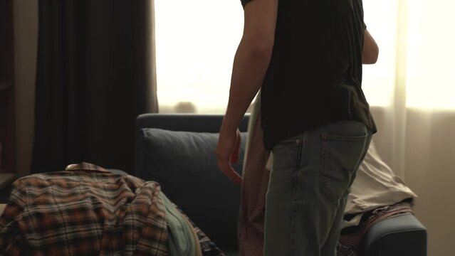 Faceless. The young man declutters his wardrobe. He swaps summer clothes for winter on hanger. Home routine. housework and housekeeping concept. 4k footage