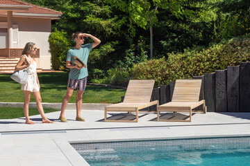 Young heterosexual couple arriving at the pool for a swim in the middle of summer with greenery around