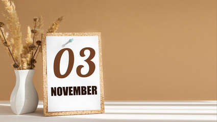november 3. 3th day of month, calendar date.White vase with dead wood next to cork board with numbers. White-beige background with striped shadow. Concept of day of year, time planner, autumn month