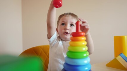 kid playing pyramid toy. happy family kindergarten kid dream concept. kid boy collects a toy pyramid of rings on a table in a kindergarten. development of fine motor skills in children lifestyle