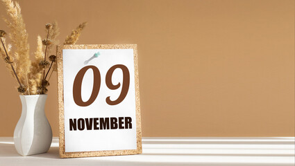 november 9. 9th day of month, calendar date.White vase with dead wood next to cork board with numbers. White-beige background with striped shadow. Concept of day of year, time planner, autumn month