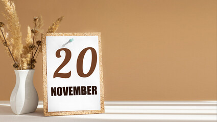 november 20. 20th day of month, calendar date.White vase with dead wood next to cork board with numbers. White-beige background with striped shadow. Concept of day of year, time planner, autumn month