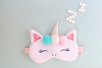 Flat lay of cute fluffy sleeping mask looks like a unicorn on blue and purple background with copy space with pills against insomnia, comfortable sleep concept