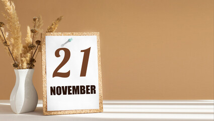 november 21. 21th day of month, calendar date.White vase with dead wood next to cork board with numbers. White-beige background with striped shadow. Concept of day of year, time planner, autumn month